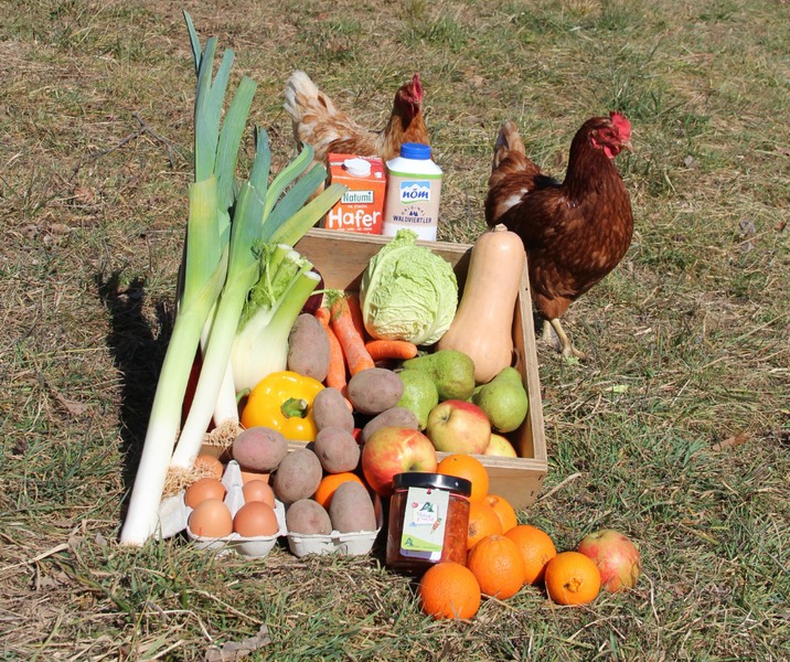 KI generiert: Eine Holzkiste voller frischem Gemüse, Obst und Eiern, daneben laufen zwei Hühner.